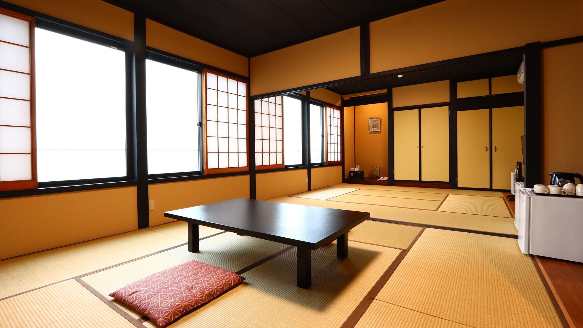 A traditional Japanese room with tatami flooring, a low table, sliding doors, and a small refrigerator.