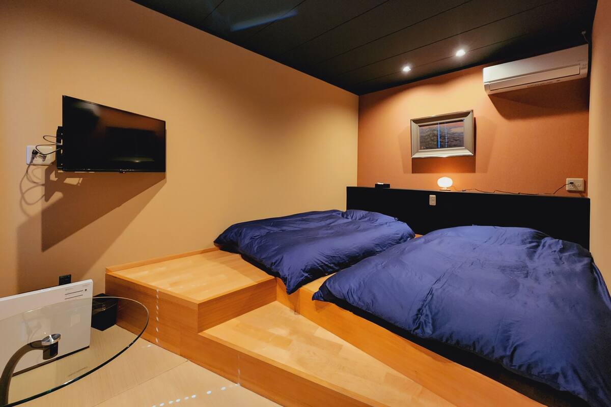 Une chambre à coucher avec un lit, un téléviseur fixé au mur et une fenêtre avec des stores.
