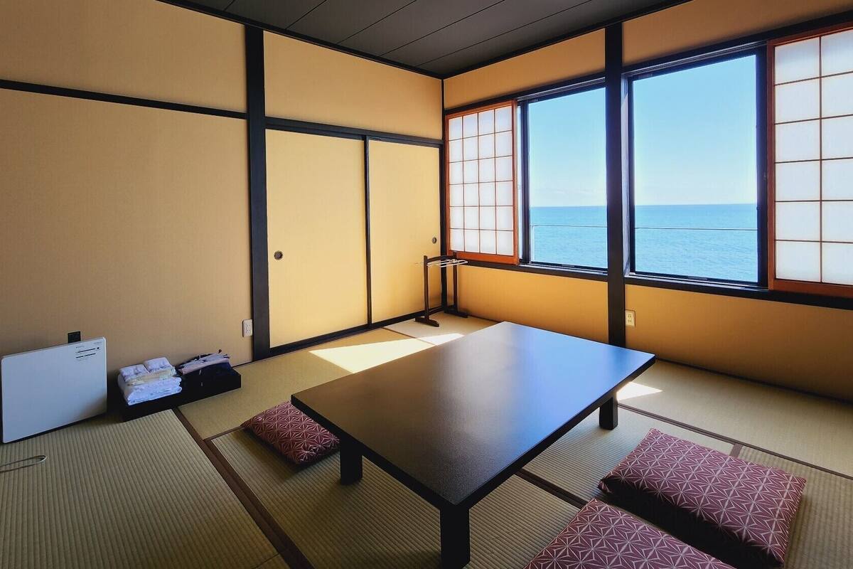 Une pièce de style japonais traditionnel, avec un sol recouvert de tatamis, une table basse et une vue sur la mer à travers des panneaux coulissants.