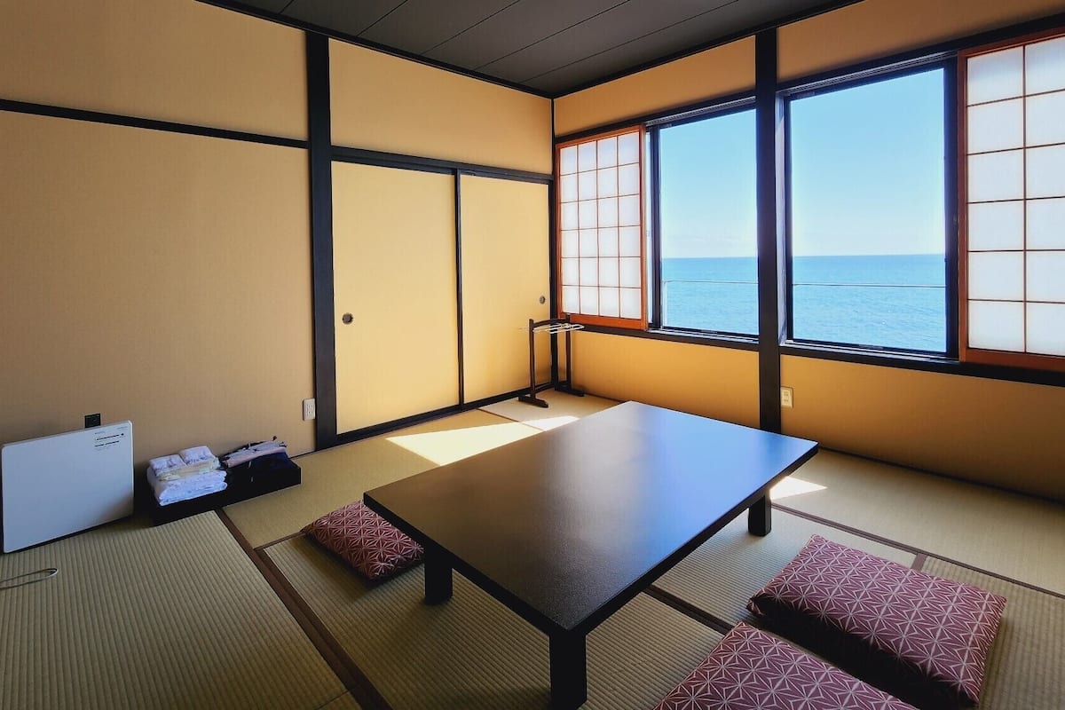 A traditional Japanese room with tatami flooring, a low table, and a view of the sea through shoji screens.