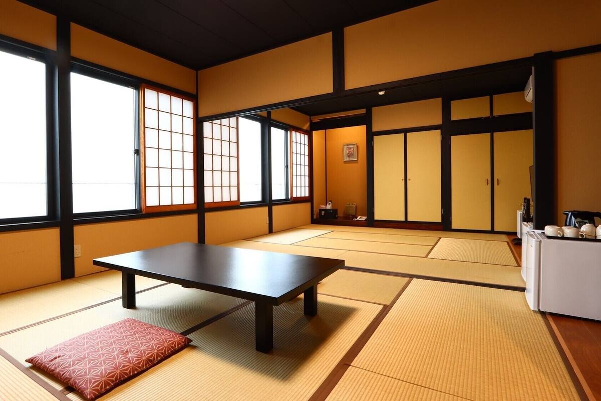 Une pièce de style japonais traditionnel, avec un sol recouvert de tatamis, une petite table basse, des portes coulissantes et un petit réfrigérateur.