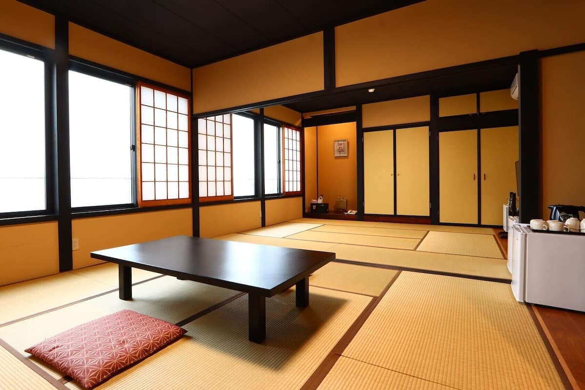 A traditional Japanese room with tatami flooring, a low table, sliding doors, and a small refrigerator.