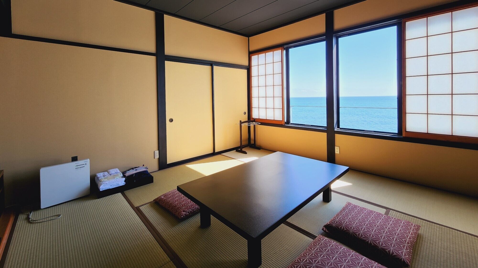 A traditional Japanese room with tatami flooring, a low table, and a view of the sea.