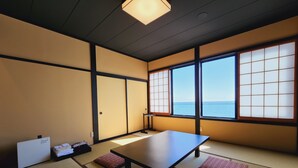 A traditional Japanese room with tatami flooring, a low table, cushions, and a view of the sea through shoji screens. - Shionomi (Himi)