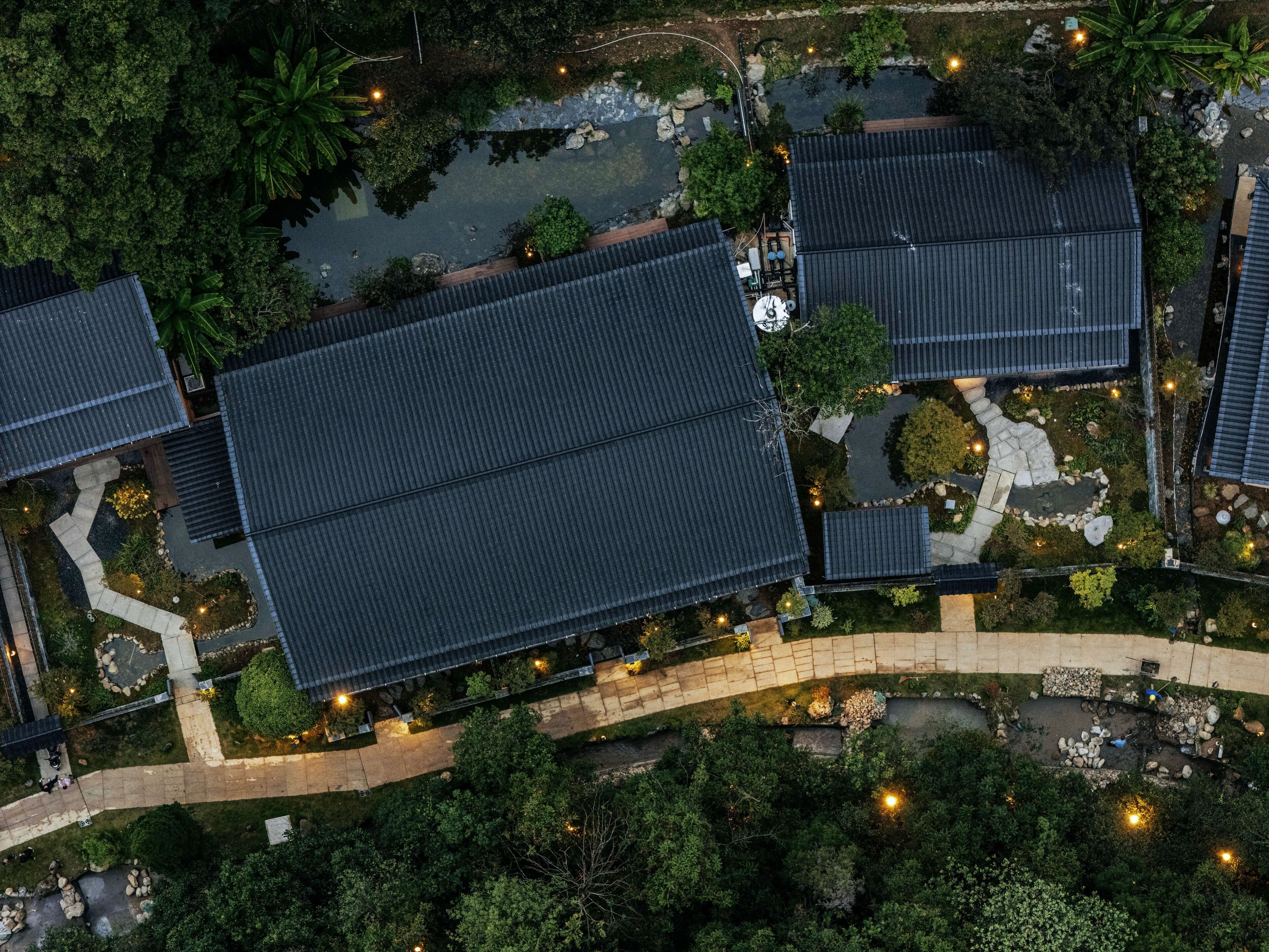 An aerial view of a residential area with multiple buildings, a pond, and well-maintained gardens.