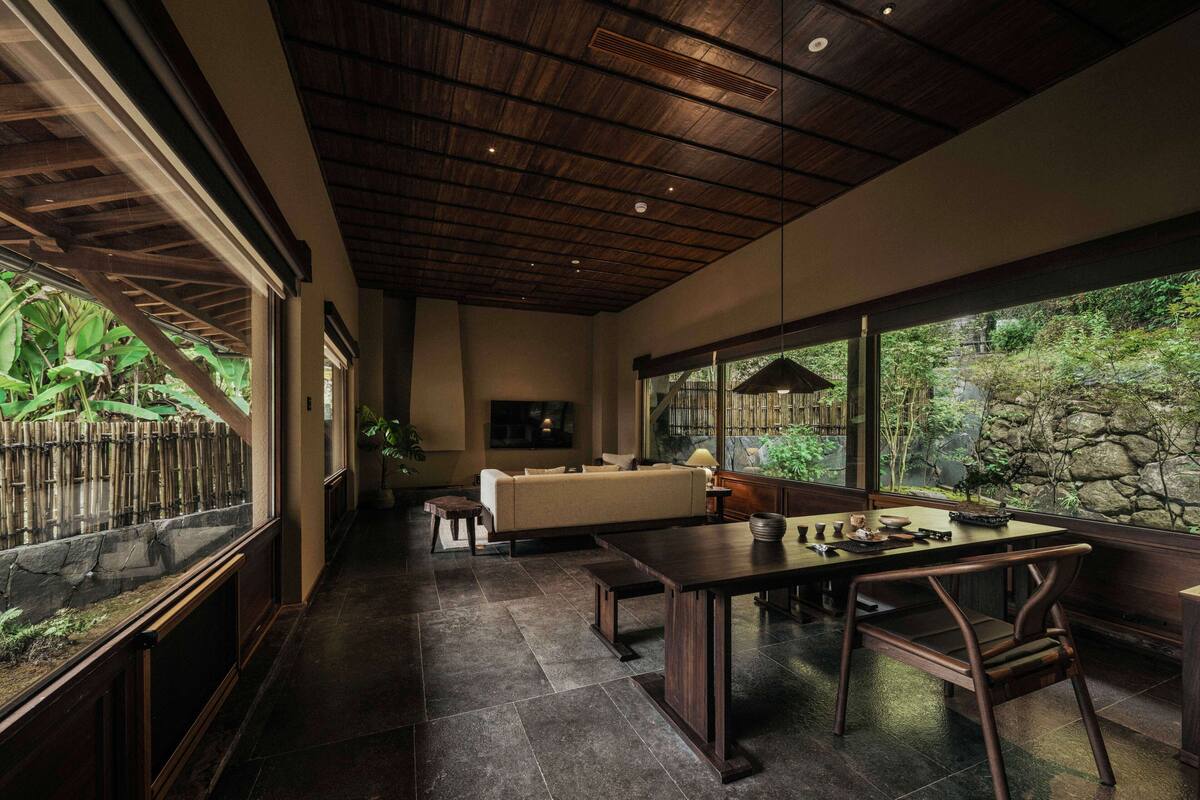 A modern interior with a dining area, a sofa, and a large window overlooking a garden.