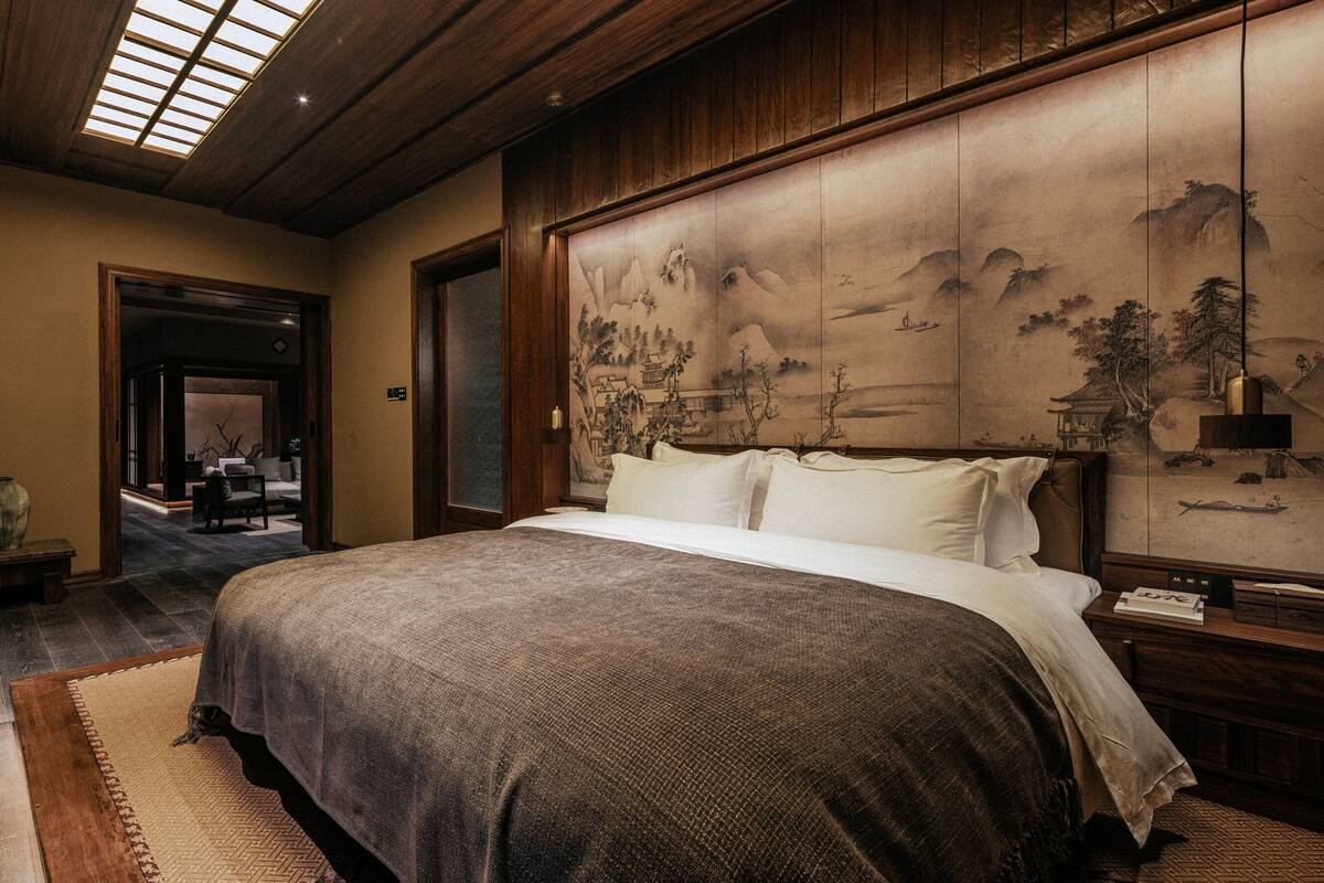 A traditional bedroom with a large bed, a wooden ceiling, and a large painting on the wall.