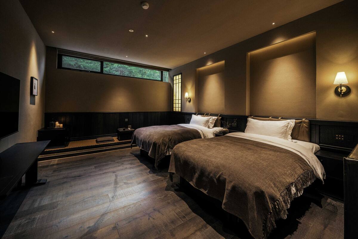 A modern hotel room with two beds, a large window, and a cozy ambiance.
