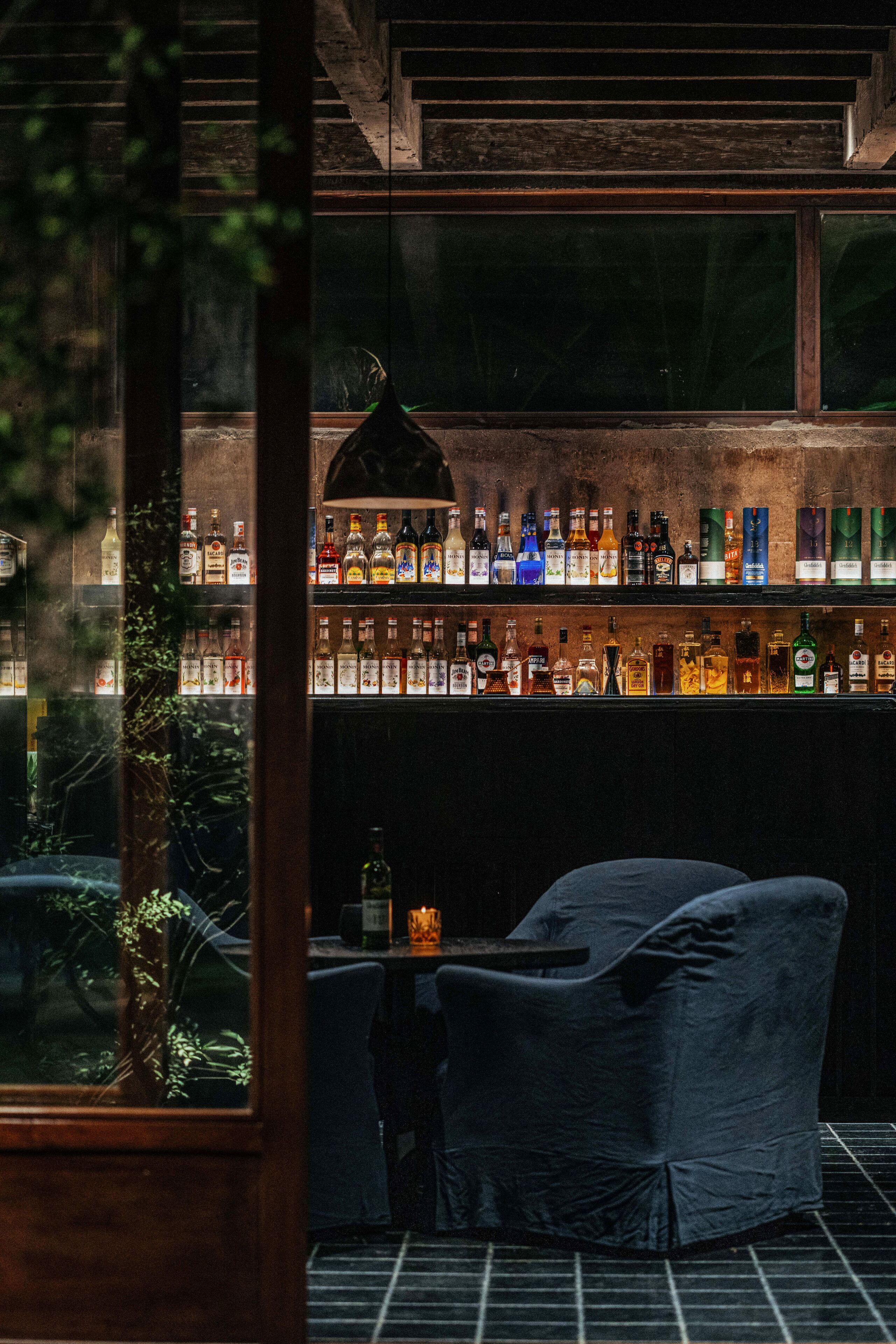A bar with shelves of liquor bottles, a hanging light fixture, and a seating area with a table and chairs.