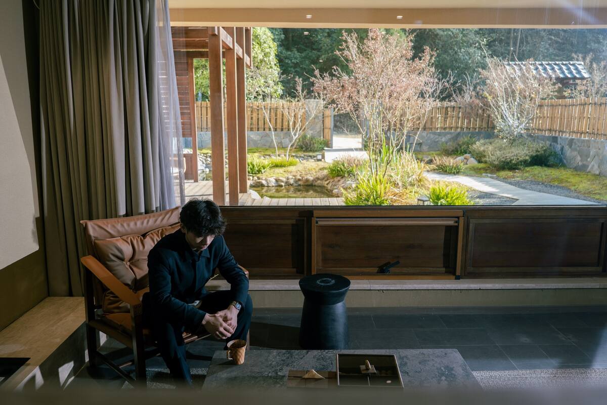 A person sitting on a chair by a window with a view of a garden.
