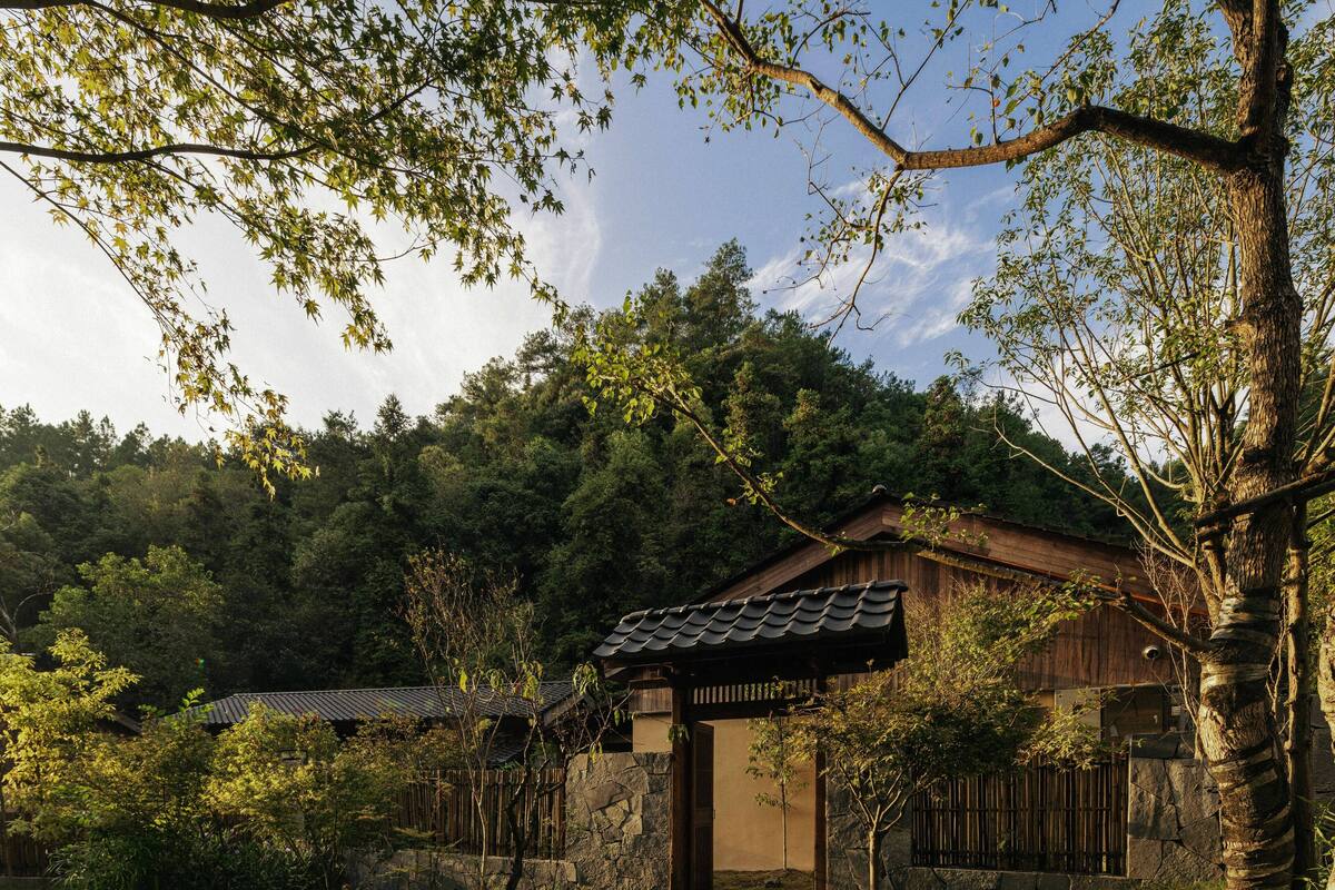A traditional Japanese-style building with a tiled roof, surrounded by lush greenery and large rocks.