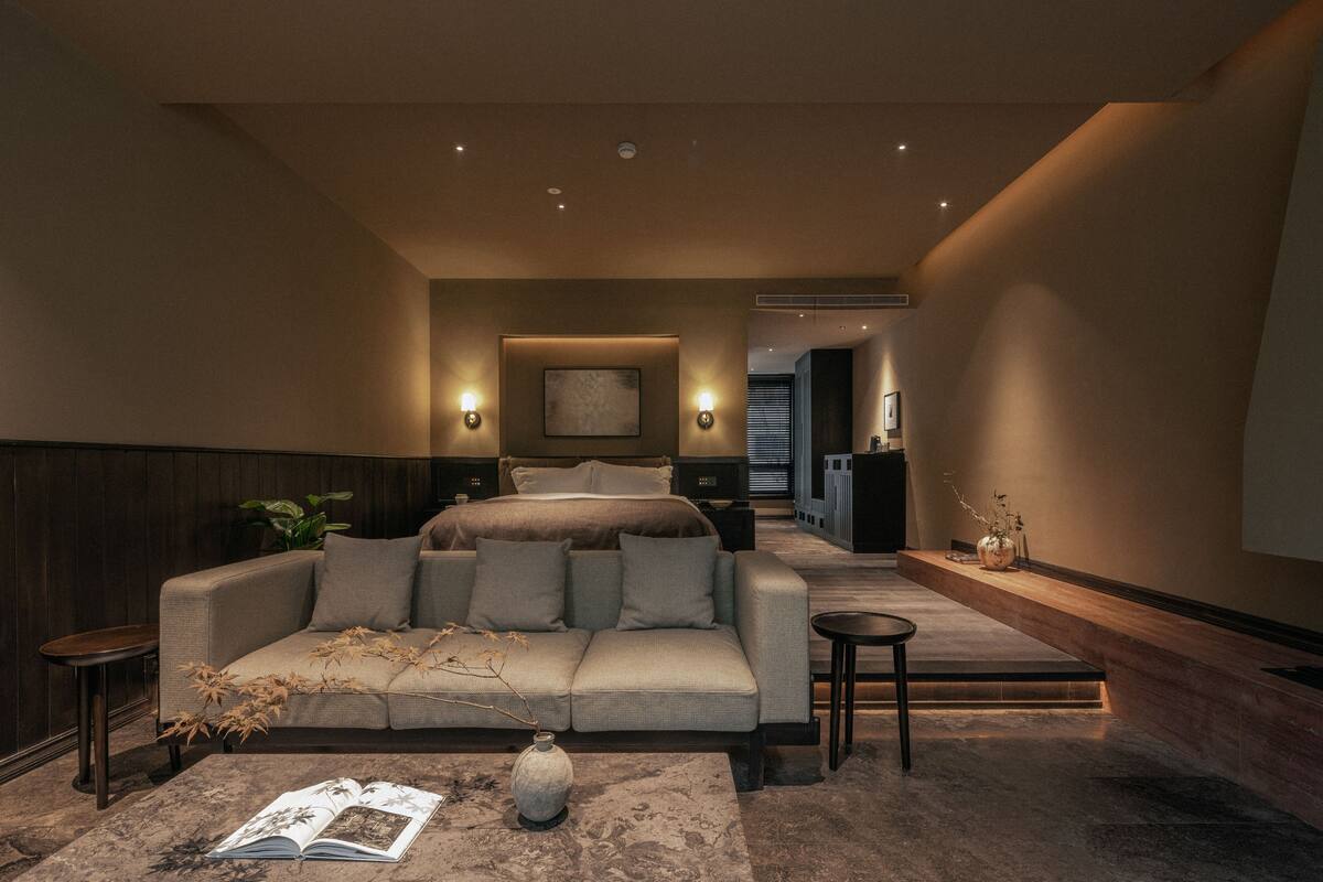 A modern hotel room with a large bed, a sofa, a small table, and a decorative vase.