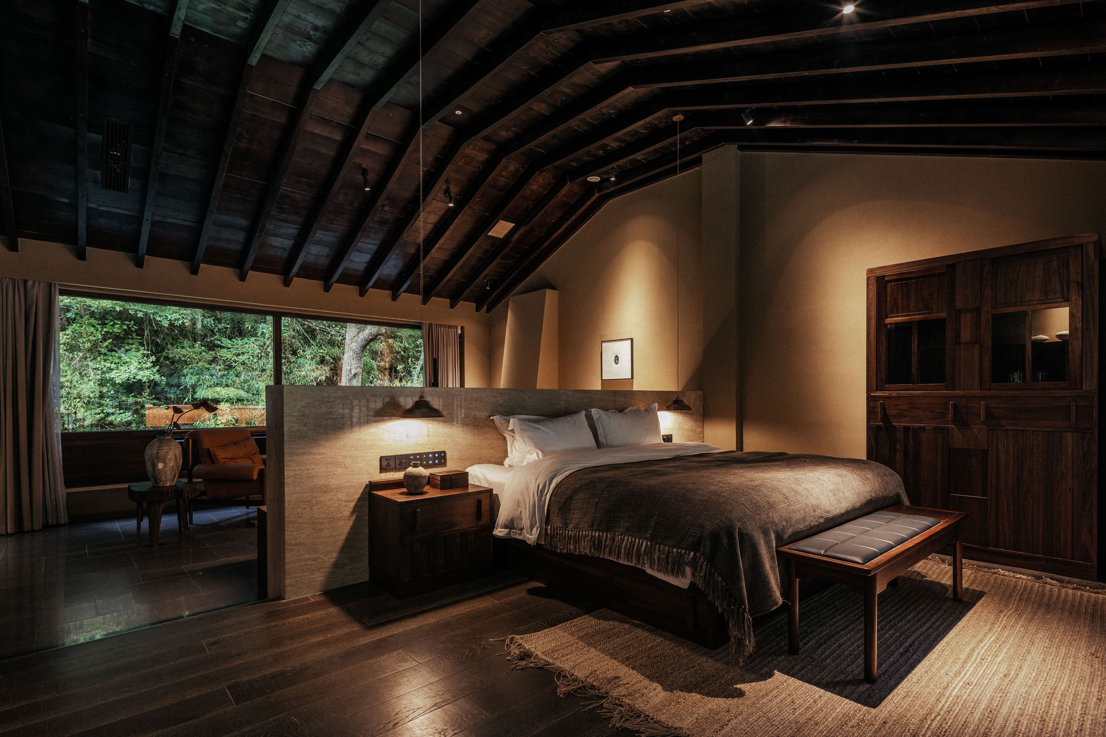 Ein Schlafzimmer mit einem großen Bett, einem Holzkopfende, Nachttischen und Blick ins Freie.