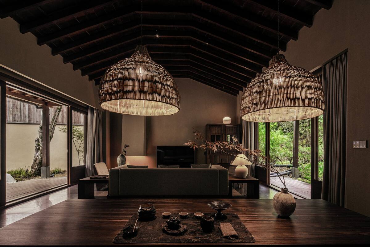 A modern living room with a large window, a sofa, a coffee table, and two hanging lamps.
