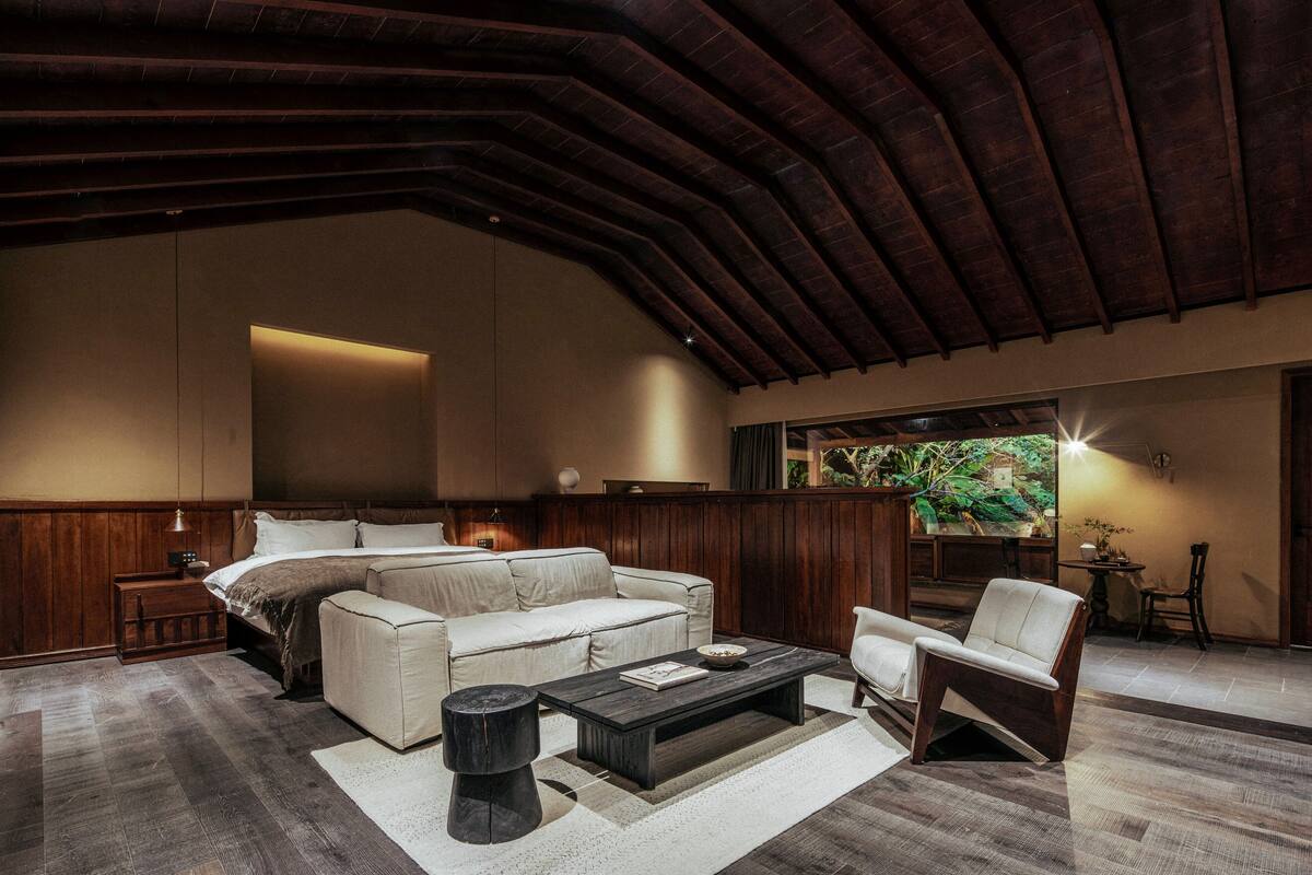 A spacious living room with a high ceiling, a large bed, a coffee table, and a seating area.