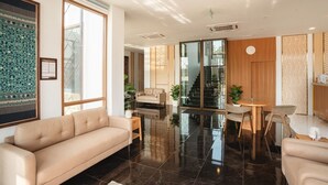 Een moderne hotel Lobby met een beige bank, een eetgedeelte met een ronde tafel en stoelen, en een trap naar een andere verdieping.
