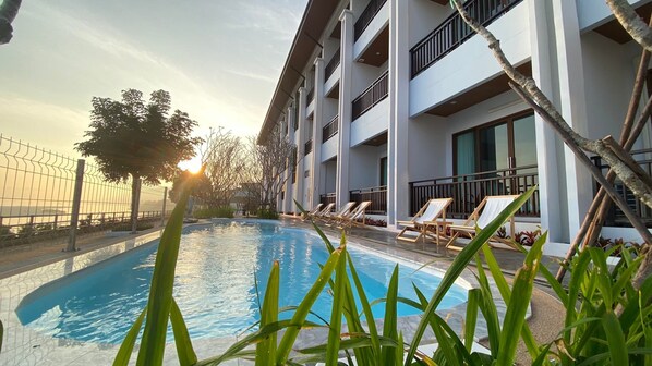 A swimming pool with lounge chairs, surrounded by a building with multiple balconies and a fence. - Sand & River Hotel (Sang Khom)