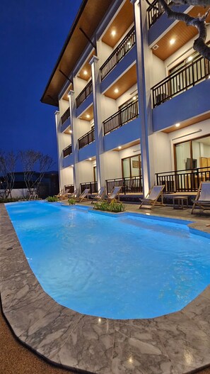 A multi-story hotel with a swimming pool, outdoor seating, and balconies.