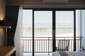 A hotel room with a large window offering a view of a river and distant hills.