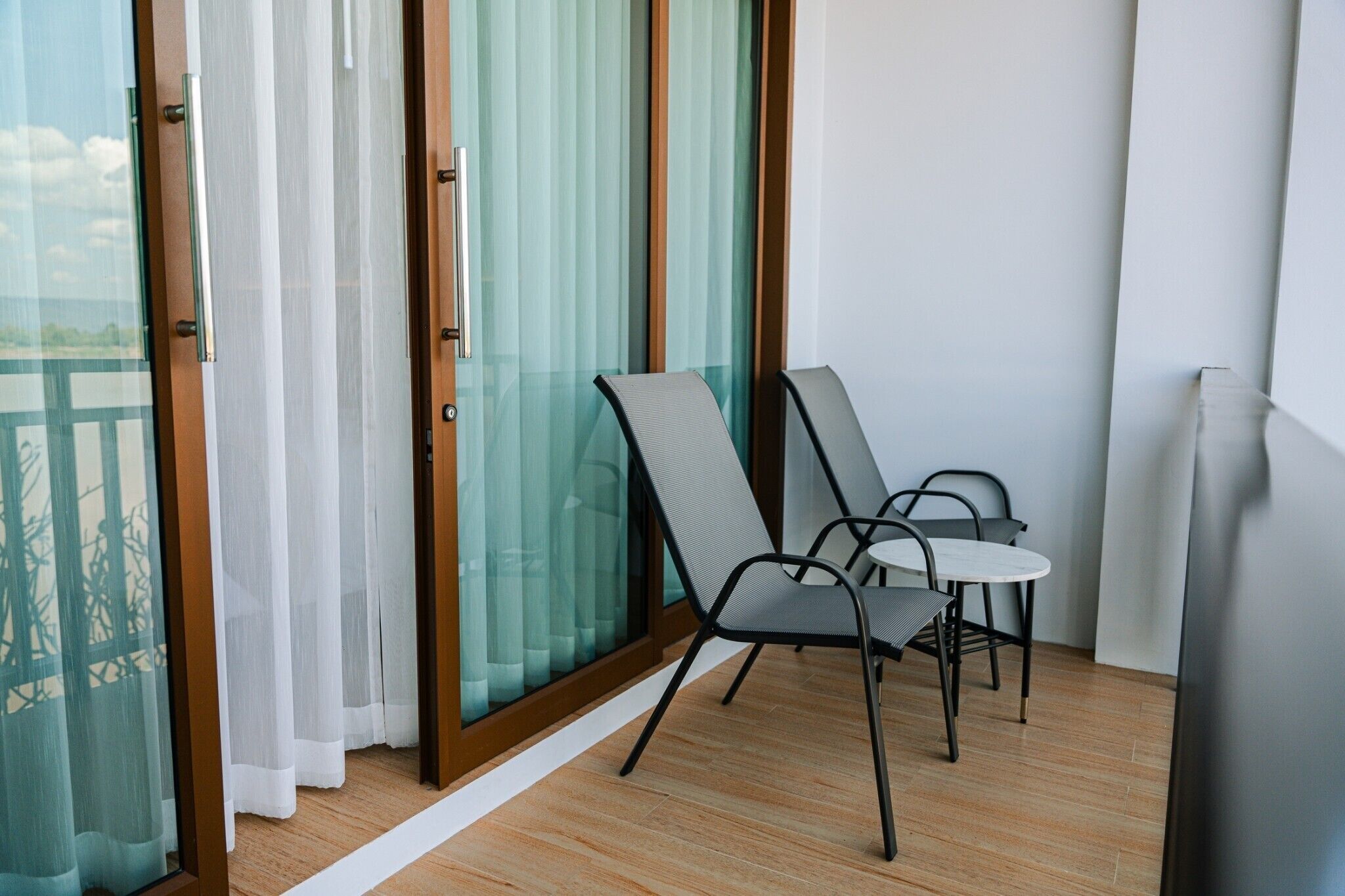 A balcony with two chairs and a table, a sliding glass door, and a view of a building.