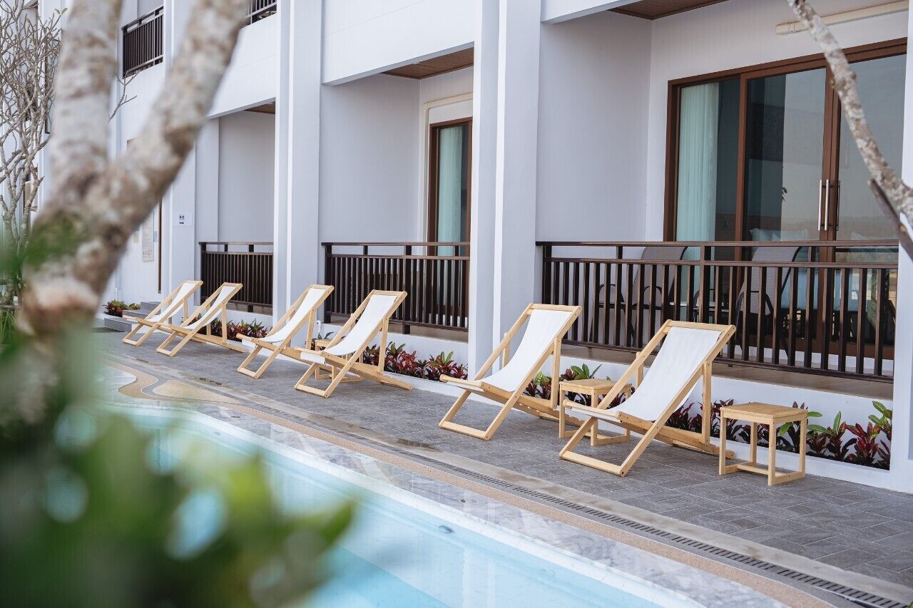 Ein Poolbereich mit Liegestühlen und einem kleinen Tisch, umgeben von einem weißen Gebäude mit großen Fenstern und einem Balkon.