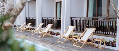 Ein Poolbereich mit Liegestühlen und einem kleinen Tisch, umgeben von einem weißen Gebäude mit großen Fenstern und einem Balkon.