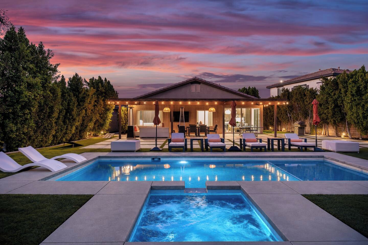 Ein Schwimmbecken mit Liegestühlen, eine überdachte Terrasse und ein Haus mit Blick zum Himmel.