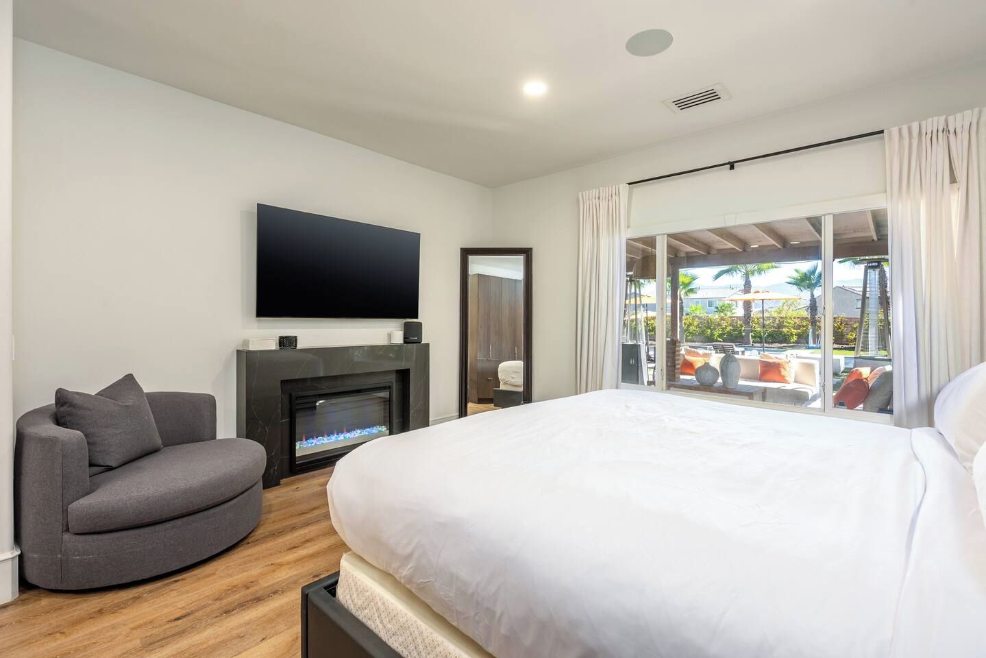 A hotel room with a bed, a sofa, a fireplace, a TV, and a balcony with outdoor seating.