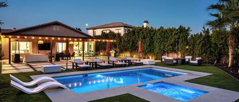 A residential swimming pool with a sunken seating area, surrounded by a well-maintained lawn and a variety of outdoor furniture.