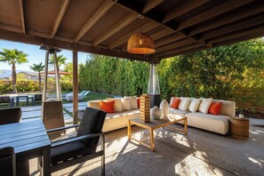 Eine Terrasse im Freien mit einem Holztisch, Stühlen, einer Couch und einer hängenden Leuchte.