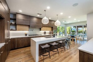 A modern kitchen with a central island, bar stools, and pendant lighting. - 4BR Desert Home: Free Heated Pool & Spa, Arcade Games, Fire Pit & Grill (Coachella)