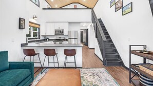 A modern kitchen with a central island, bar stools, and a staircase leading to another level. - Silent Princess, Tiny Home (Tracy City)