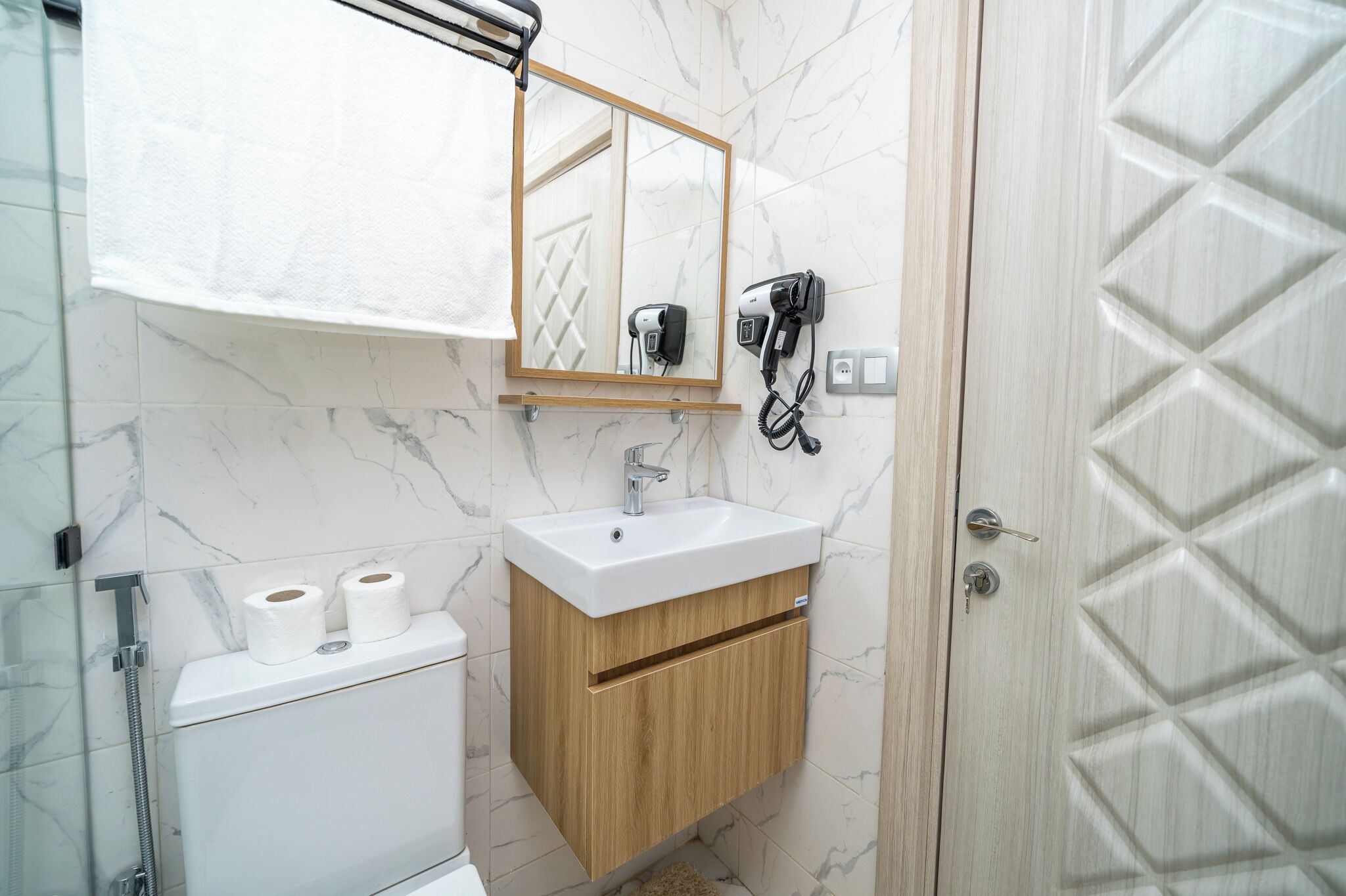 Une salle de bain avec un mur en marbre, un meuble-lavabo en bois, un évier, un miroir et un sèche-cheveux.