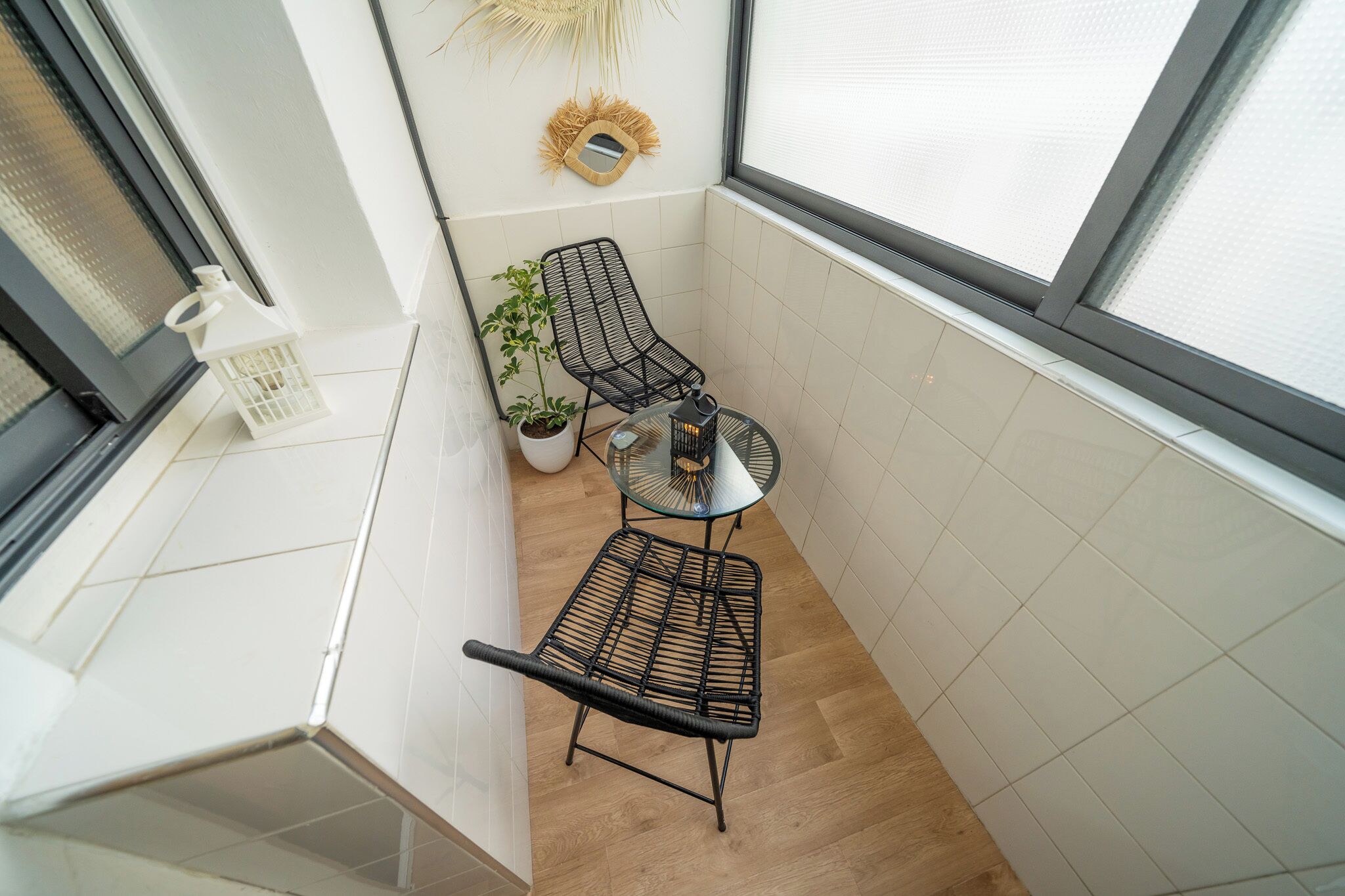 A small balcony with two black wire mesh chairs, a small round table, a potted plant, and a decorative mirror on the wall.