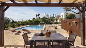A covered outdoor area with a pool, lounge chairs, and a table with chairs. - Rustic Retreat with Pool and Stunning Views (Altura)