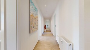 A hallway with a long view, white walls, a large abstract painting, and a radiator. - Modern, stylishly renovated 3-room apartment with balcony near the beach - (Hörnum (Sylt))