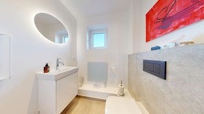 Ein modernes Badezimmer mit rundem Spiegel, Waschbecken, Toilette und Duschbereich.