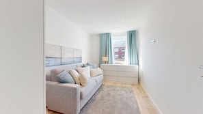 A modern living room with a sofa, a side table, and a view through a window with curtains. - Modern, stylishly renovated 3-room apartment with balcony near the beach - (Hörnum (Sylt))
