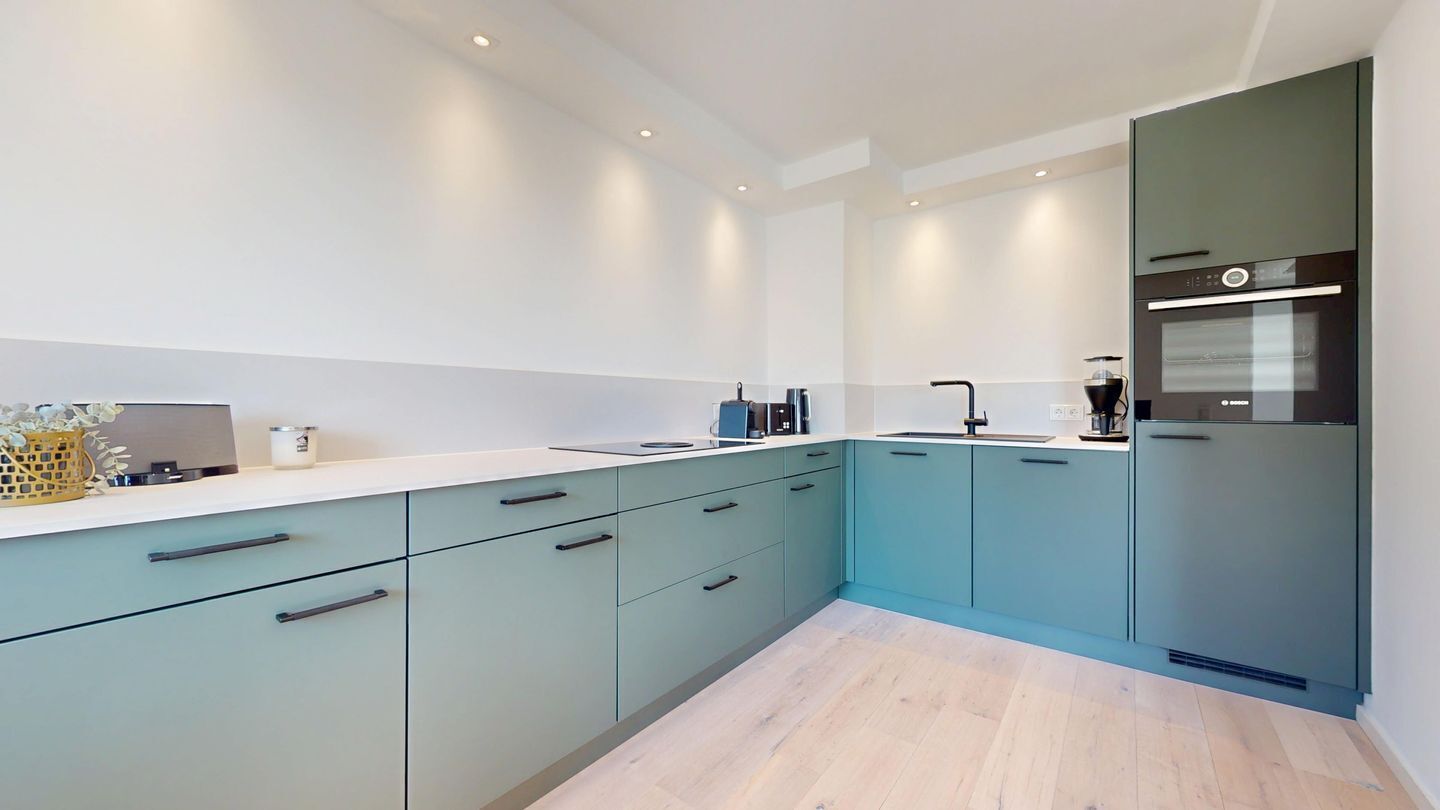 A modern kitchen with teal cabinets, a white countertop, and a built-in oven.