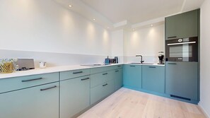 A modern kitchen with teal cabinets, a white countertop, and a built-in oven. - Modern, stylishly renovated 3-room apartment with balcony near the beach - (Hörnum (Sylt))