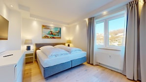Ein Schlafzimmer mit Bett, Nachttischen, einem Gemälde und einem Fenster mit Vorhängen.