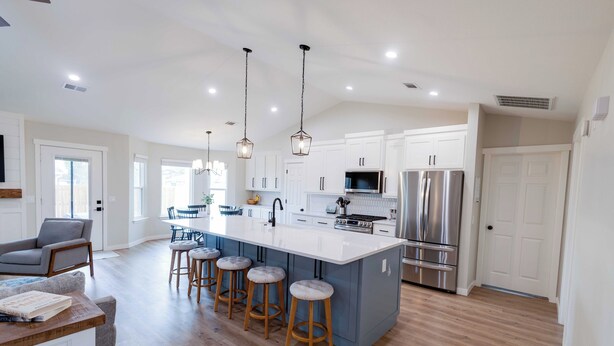 A modern kitchen with a large island, stainless steel appliances, and wooden stools. - The Coler House - Near Coler Bike Trails (Bentonville)