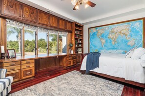 A bedroom with a large bed, wooden cabinetry, a world map on the wall, and a view of greenery outside.
