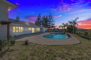 A house with a swimming pool, a brick exterior, and a large tree in the backyard.