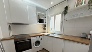 Une cuisine moderne avec des armoires blanches, un plan de travail en bois, un four encastré, un lave-linge et une fenêtre au-dessus de l’évier.