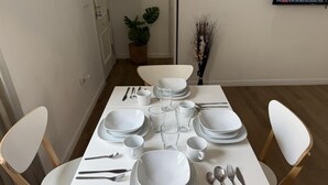 Une table à manger dressée avec des assiettes, des bols, des verres et des couverts blancs.