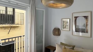 Une chambre avec un balcon, un luminaire en fibres tressées et des œuvres d’art encadrées accrochées au mur.