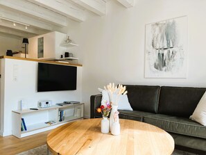 Uma sala de estar moderna com uma mesa de centro de madeira, um sofá de couro preto, uma televisão de tela plana na parede e uma obra de arte minimalista.