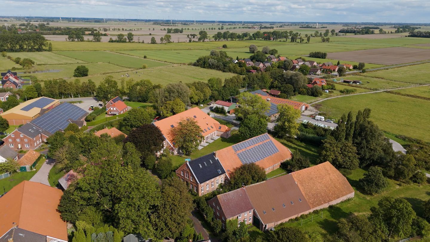 Vue aérienne d’un village rural avec des maisons, des panneaux solaires et des champs verdoyants.
