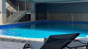 A swimming pool with a tiled edge, a staircase leading to an upper level, and a lounge area with a chair.